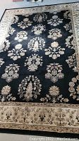 Full view of the black area rug with cream floral patterns and a decorative border, showing the size and overall design.