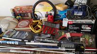 Photo showing Wen orbital waxer box with power cord at upper right, steering wheel cover in center, assorted automotive cleaning products including Mother's and Armor All brands, and jumper cables coiled at the bottom center.
