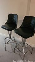 Pair of black vinyl bar stools with metal bases showing front and side angles