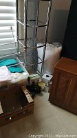 Chrome etagere, towels in tote, oak hamper, and other items on floor near window.