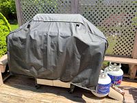 Covered BBQ grill with two visible propane tanks and a gas meter on a wooden patio deck