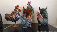Wood and metal painted chicken and rooster figurines arranged on a surface showing size variations and details.