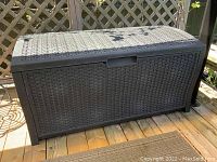 Side view of the brown plastic wicker design deck box placed on a wooden deck