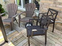 Photo showing two dark brown Muskoka chairs and two dark brown stacking dining chairs with arms on a wood deck, plus outdoor clock