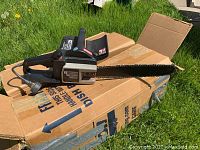 Mastercraft MC2500 electric chainsaw resting on cardboard outdoors on grass, showing full length with chain and power cord.