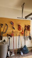 Multiple tools hung on pegboard, including trimmers, forks, shovels, rake, cords