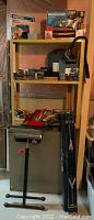 Full view of shelves containing various tools including a red tray with hand tools, metal folding saw horses leaning against a grey surface, and other assorted items.
