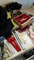 Overview of drawer with red and white utensils, knife storage box, folded towels, placemats