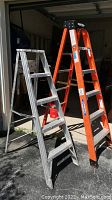 Two ladders side by side; a silver 5ft aluminum ladder and an orange 6ft Werner fiberglass ladder.