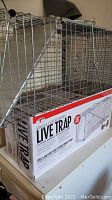 Photo of two wire mesh single-door live traps stacked with packaging box visible underneath showing trap dimensions and usage instructions.