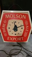 Front view of square Molson Export light up clock, showing red and white face with ship logo and electric cord.