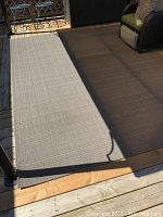 Woven outdoor rug on wooden deck, showing size and color under natural daylight.