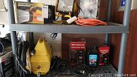 Photo showing Karcher 410 pressure cleaner, Motomaster hydraulic jacks and oil, Coleman spotlight box, orange extension cord, and other items on shelving.