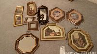 Overview of 11 small framed wall decorations laid on floor including mirrors and prints of various sizes and shapes