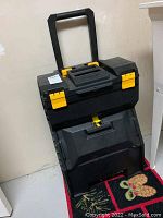 Full front view of the Stanley rolling tool box with folding handle extended, showing yellow latches and main compartments.