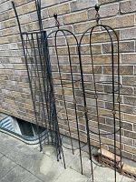 Two metal arched obelisks and two curved X-design trellis panels leaning against brick wall