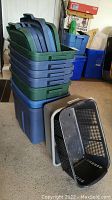 Stack of seven Rubbermaid Roughneck blue totes with green lids and two open bins, black and gray, on ground.