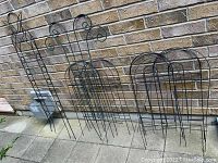 Full view of 6 pieces of black metal garden edging and trellis against a brick wall on patio, showing size and shape of each piece.