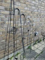 Photo showing metal shepherd's hook, tall round obelisk, metal garden decor shaped like a tea pot, and multiple metal trellises with geometric patterns
