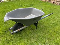 Full side view of grey plastic Garant wheelbarrow with black single tire and metal arms, resting on grass.