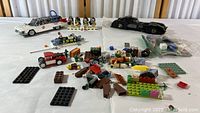 Photo showing the Ghostbusters Ecto-1 car, Batman Batmobile, and various loose Lego bricks and figures scattered on a white surface.