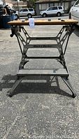 Front view of Black and Decker Workmate folding workstation showing metal frame, wooden top with holes, and step base.
