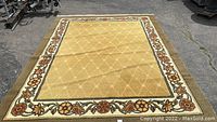 Full view of large rectangular gold area rug with floral border showing overall design and condition