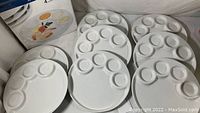 Set of eight white stoneware fondue plates stacked and displayed on a surface showing the seven-well design on each plate.