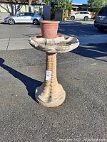 Front-right view of the concrete bird bath with terracotta planter pot placed in the basin's center.