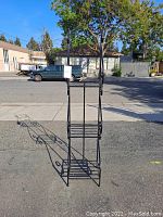Full view of black metal 3 shelf plant stand showing its height and proportions outdoors.