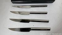 Four Retroneu steak knives with stainless steel handles and blades, laid out side by side showing cutting edges and full length.