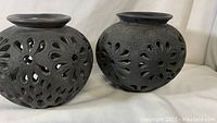 Pair of dark composite pots with detailed flower cut-out designs seen from the side, showing texture and form.