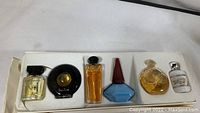 Top view of six miniature perfume bottles inside original compartmentalized white box showing sizes and bottle designs.