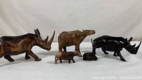 Full frontal view of the five wooden animal figurines showing two rhinos, water buffalo, and two antelopes with varying shades and sizes.