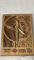 Front view of wooden wall clock showing detailed laser engraving of Joe Montana in 49ers gear with NFL and Super Bowl logos.