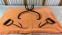 Photo of the vintage ice tongs and two hooks on an orange towel, showing their size, shape, and surface wear.
