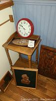 Wooden accent table with several framed pictures, carved plaque and round clock on top, and smaller framed pictures leaning around the table.
