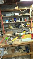 Workbench and shelves with assorted workshop and painting supplies including containers, masking tape, and miscellaneous hardware.