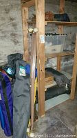 Overall view of camping supplies including foldable chairs in carrying bags, tarps on wooden shelf, and storage bins in cellar area