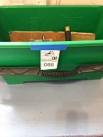Green plastic rubber tub with handle, partially filled with cleaning items