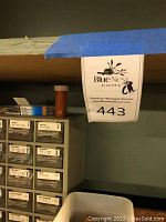 Shelf with small drawer cabinets labeled with various fasteners including screws, nuts, washers in different sizes and types, with a tag 'Blue Nose Home 443'.