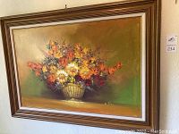 Full view of framed floral oil painting featuring mixed colorful flowers in a wicker basket on a greenish-brown background.