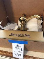 Photo showing a gold-colored faucet in a box labeled 'Sign of the Crab'. Box contains foam packaging and some attachments.