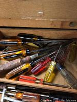 Drawer with assorted screwdrivers in various handle colors including amber, red, yellow, and black, some with wooden grips.