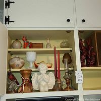 Full view of shelf with various collector items including angel figurine in center, candles, pottery, bird figurine, and oil lamp.