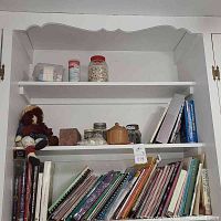 Bookshelves stocked with sewing books, magazines, jars of buttons, wooden container, and a doll on the left side