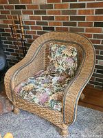 Front view of the wicker armchair with floral cushions, showing the woven texture and carved leg detail.
