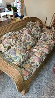 Wicker arm sofa with floral cushions and throw pillows in a room setting.