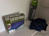 Two blue flocked single air mattresses, one folded and one boxed, with a green hand pump next to them.
