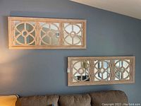 Two wooden-framed rectangular mirrored wall art panels with circular geometric wooden overlays hung on a blue-gray wall.